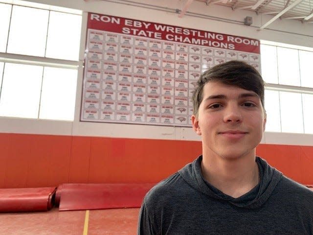 Gabe Giampietro stands in the Ron Eby Wrestling Room in front of the Smyrna wall of state champions.