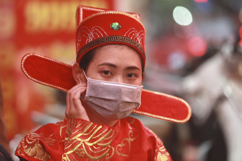 A woman in costume of the Prosperity and Wealth God wears a protective face mask at a gold shop in Hanoi, Vietnam, Monday, Feb. 3, 2020. It is a tradition for many Vietnamese to buy gold on the tenth day of the lunar new year - the day of Prosperity and Wealth God, for good luck. (AP Photo/ Hau Dinh)