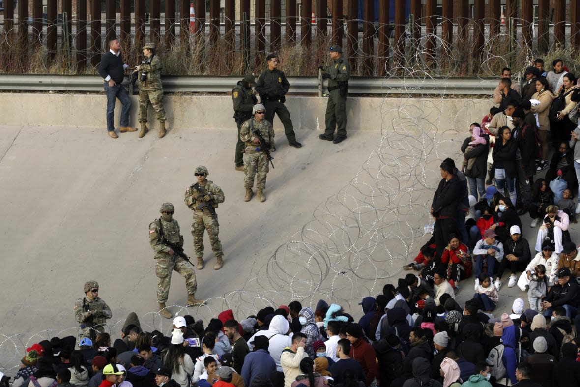 Migrants congregate on the banks of the Rio Grande at the U.S. border with Mexico on Tuesday, Dec. 20, 2022, where members of the Texas National Guard cordoned off a gap in the U.S. border wall. (AP Photo/Morgan Lee)