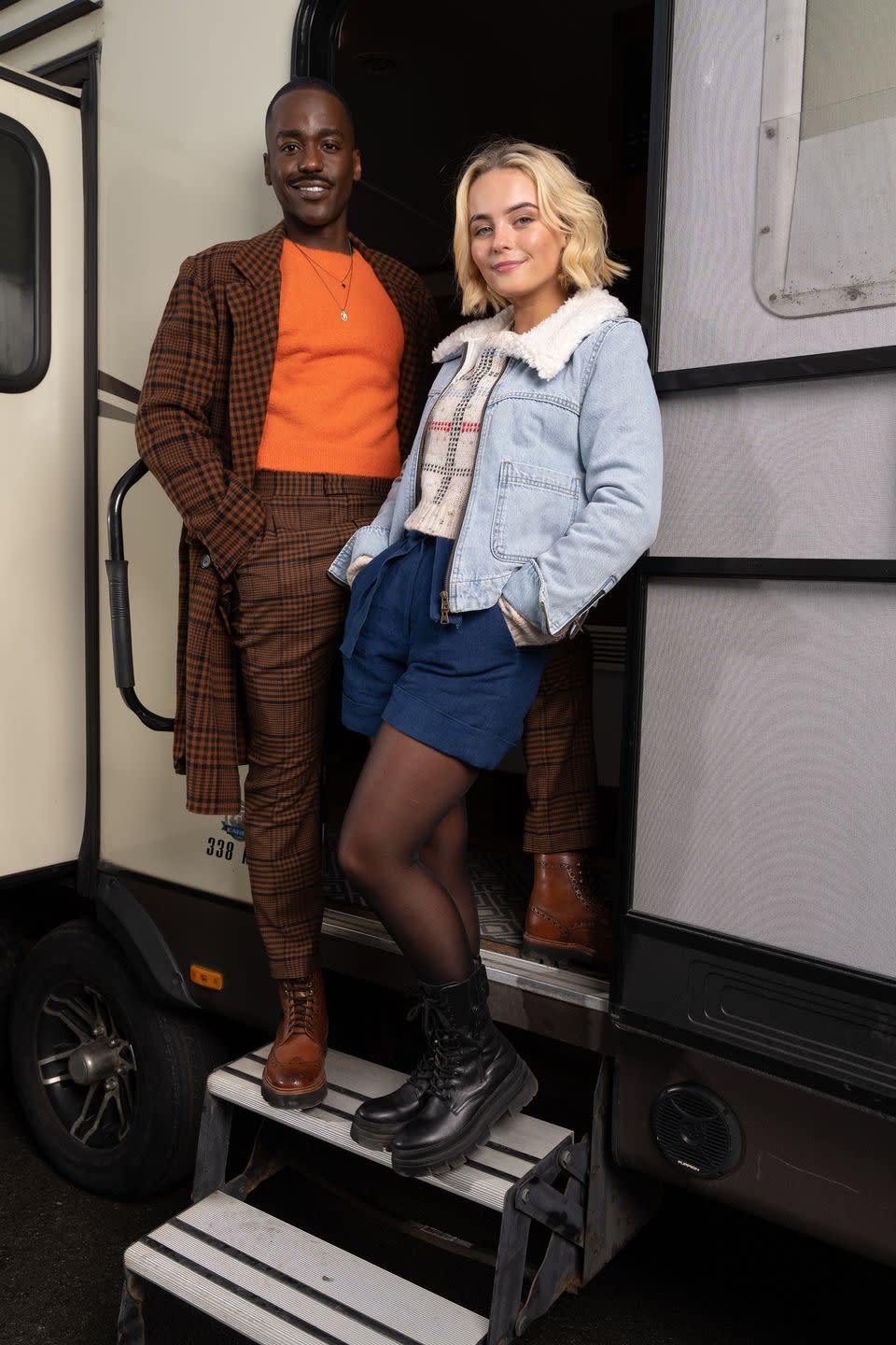 doctor who stars ncuti gatwa and millie gibson in costume on set, posing on the steps of a trailer for a first look photo