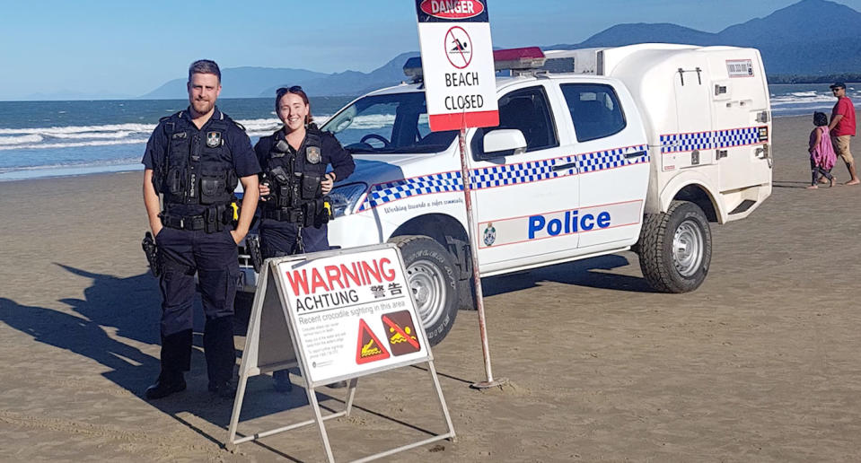 Two police officers stand on Four Mile Beach, Port Douglas, on Tuesday with a sign telling beachgoers the beach has been closed due to a crocodile sighting.