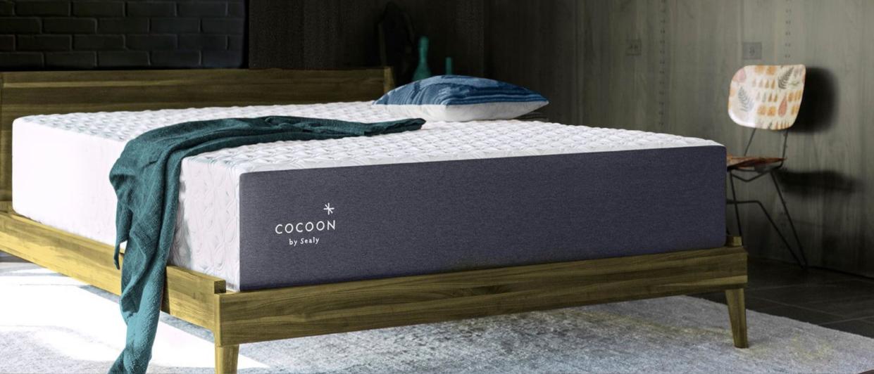  The Cocoon by Sealy Chill mattress placed on a wooden bed frame against a dark wall d across it. 