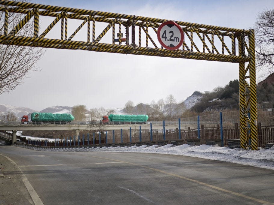 Trucks crossing a bridge in the background and a height-restriction barrier in the foreground covered in black-and-yellow tape.