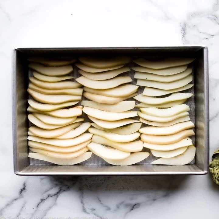 sliced pears lined vertically in a square metal baking tray