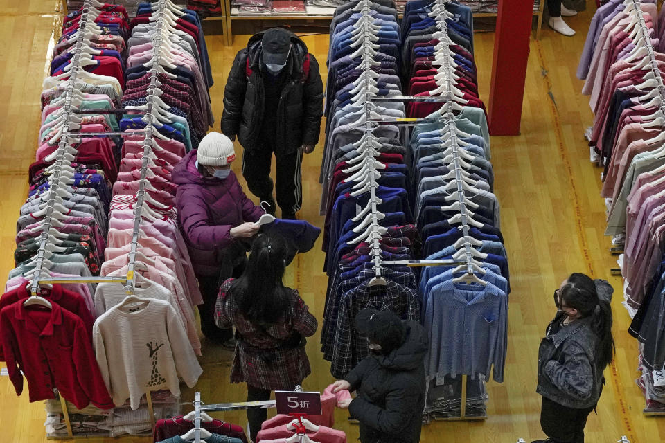 FILE - People wearing face masks shop clothing during a promotion New Year sale at a mall in Beijing on Jan. 16, 2022. China’s economic growth edged up to a still-weak 4.8% over a year earlier in the first three months of 2022 as spreading coronavirus outbreaks prompted shutdowns of major industrial cities. (AP Photo/Andy Wong, File)