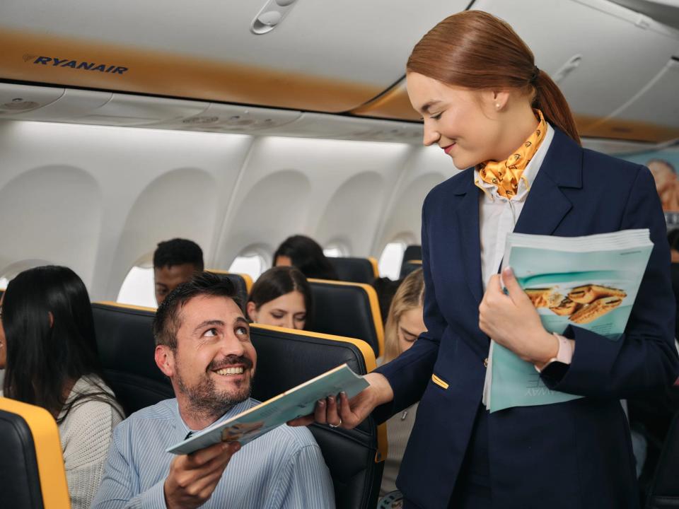 A Ryanair flight attendant passes magazine to a customer sitting on board a plane.
