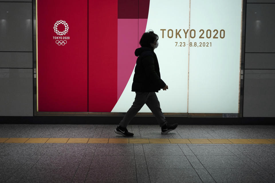 Una mujer con mascarilla camina frente a un anuncio de los Juegos Olímpicos enTokio, el 6 de abril de 2021 (AP Foto/Eugene Hoshiko)