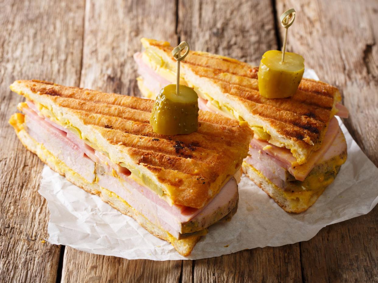 Cuban sandwich with ham, mustard, cheese, pickled cucumbers and pork close-up on paper on the table. Horizontal