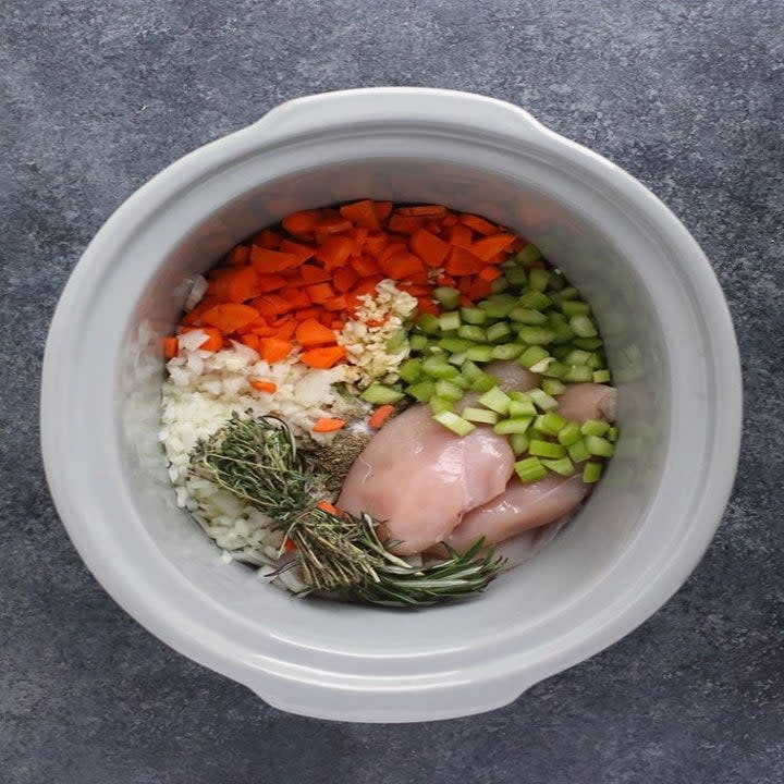 Chicken and diced carrots, celery, and onion in a slow cooker with a bundle of spices