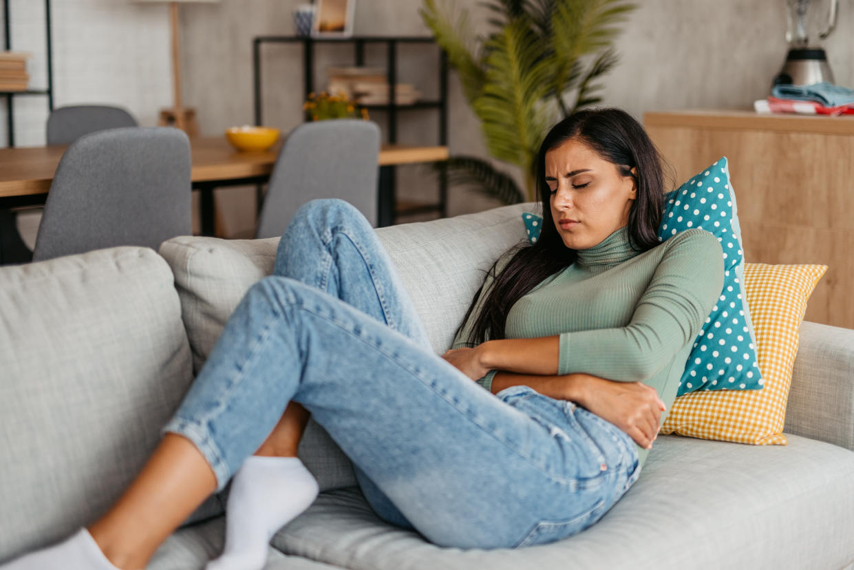 Young woman lying on the sofa and having period cramps. PCOS
