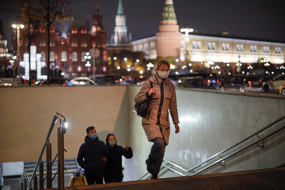 A woman wearing a face mask to help curb the spread of the coronavirus walks from the underpass under the street with the Historical Museum and the Kremlin are in the background in Moscow, Russia, Tuesday, Nov. 3, 2020. Russia reported more than 18,000 daily coronavirus cases for a record five straight days. However, authorities have resisted a second lockdown or shutting down businesses despite reports about overwhelmed hospitals, drug shortages and inundated medical workers. (AP Photo/Alexander Zemlianichenko)