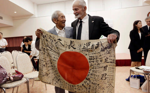 WWII veteran Marvin Strombo, right, and Tatsuya Yasue, 89-year-old farmer, hold a Japanese flag with autographed messages which was owned by his brother Sadao Yasue, who was killed in the Pacific during World Work II, during a ceremony in Higashishirakawa, in central Japan's Gifu prefecture - Credit: Eugene Hoshiko /AP