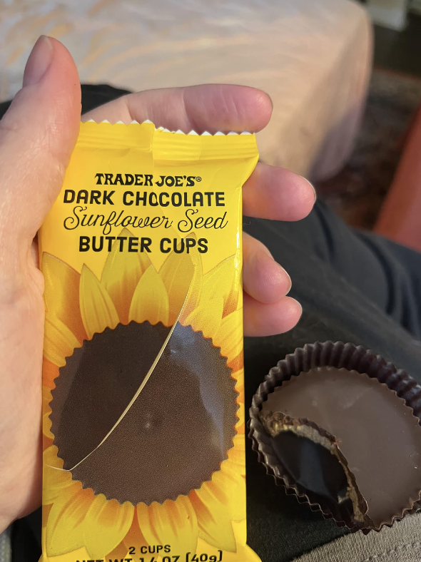 Hand holding Trader Joe's Dark Chocolate Sunflower Seed Butter Cups with one unwrapped, showing filling