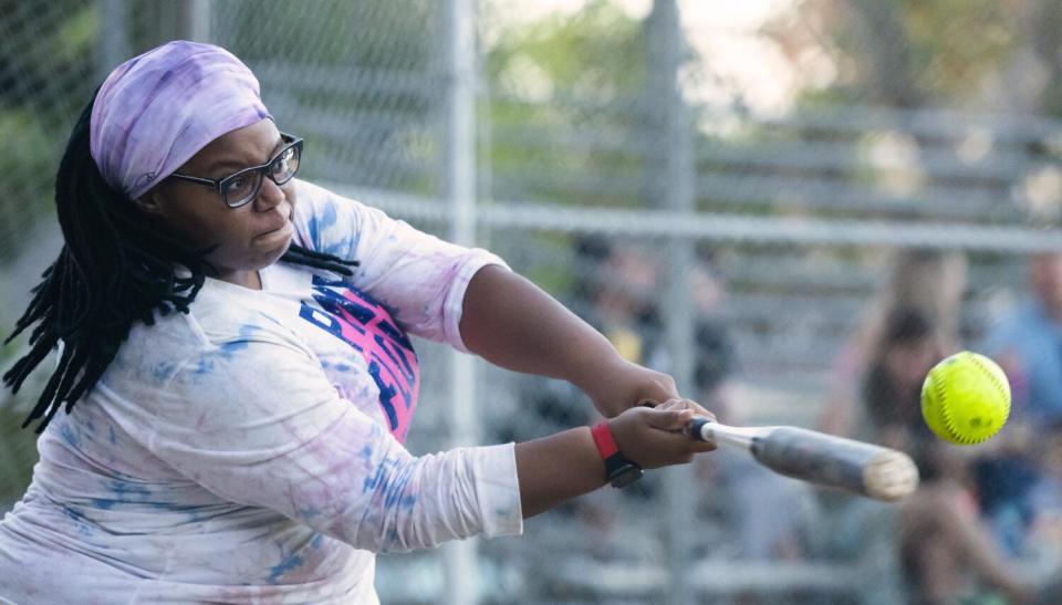 A person swings a bat at a green softball.