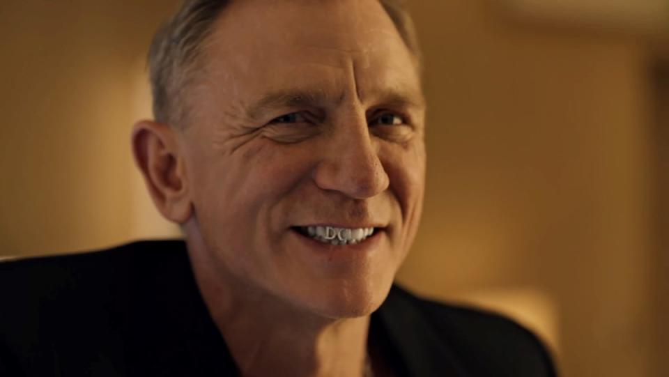 Daniel Craig smiling with a diamond DC in his teeth