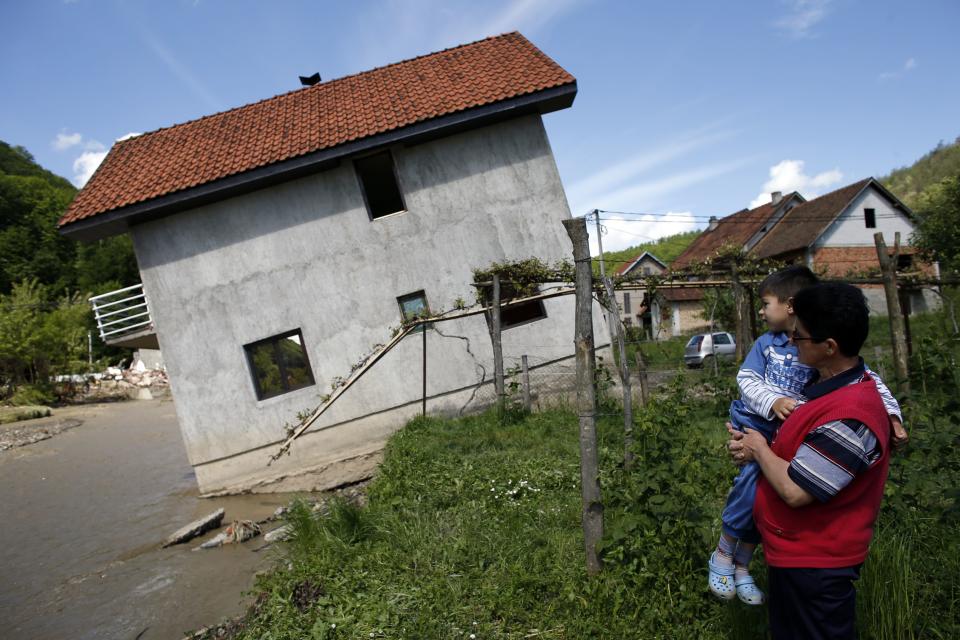 A woman with a child looks at tilted house in the village of Krupanj