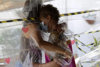 FILE - In this Jan. 6, 2021, file photo, Maria Amelia, right, hugs her niece Flaviana Silva through a plastic barrier during a visit to the Casa Clara home for the elderly in Brasilia, Brazil. The global death toll from COVID-19 has topped 2 million. (AP Photo/Eraldo Peres, File)