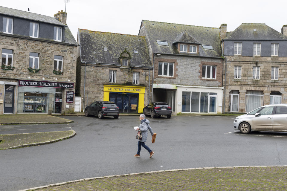 A woman holds some bread as she crosses the street in the village of Callac, on Dec.15, 2023. The far right cried victory in January 2023, when mayor Jean-Yves Rolland of Callac gave up his plan to house seven to 10 refugee families. (AP Photo/Mathieu Pattier)