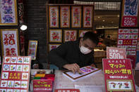 In this Feb. 13, 2020, photo, a vendor wears a mask while writing calligraphy for customers in Yokohama's Chinatown, near Tokyo. A top Olympic official made clear Friday the 2020 Games in Tokyo will not be cancelled despite the virus that has spread from China. (AP Photo/Jae C. Hong)