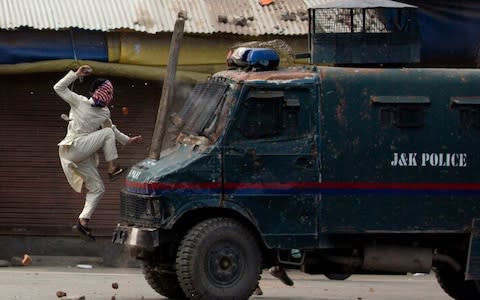 A masked Kashmiri protester jumps on the bonnet of an armored vehicle of Indian police as he throw stones at it during a protest in Srinagar, Indian controlled Kashmir, Friday, May 31, 2019.  - Credit: AP