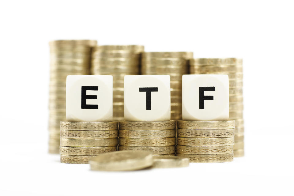 The letters ETF (Exchange Traded Fund) on lettered dice on stacks of gold coins on a white background.