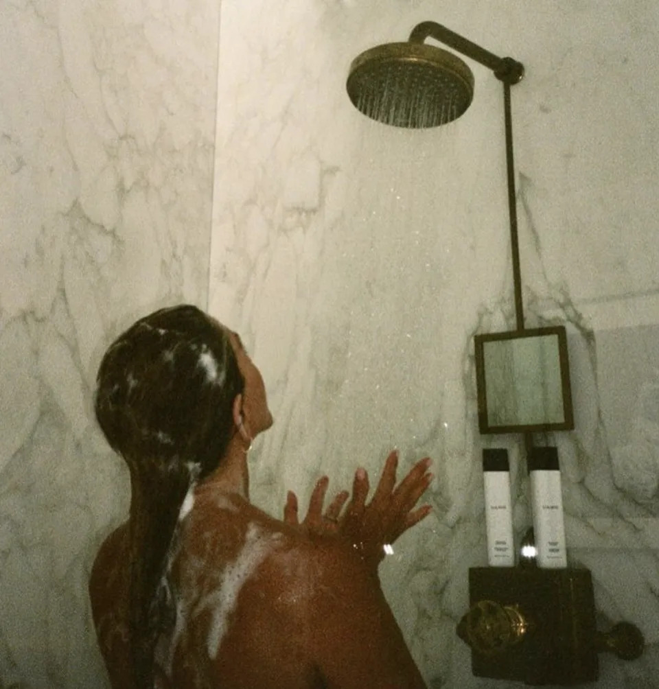 Jennifer Aniston stands in the shower lathered up with soap. 