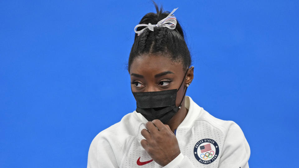 Simone Biles, of the United States, stands wearing a mask after she exited the team final with apparent injury, at the 2020 Summer Olympics, Tuesday, July 27, 2021, in Tokyo. The 24-year-old reigning Olympic gymnastics champion Biles huddled with a trainer after landing her vault. She then exited the competition floor with the team doctor. (AP Photo/Natacha Pisarenko)