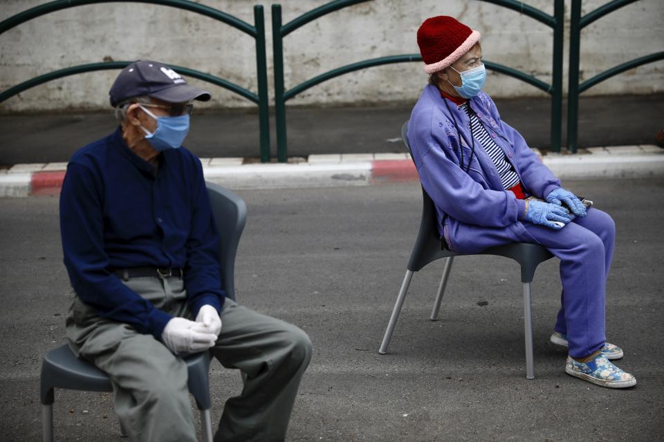 Holocaust survivors Manya Herman, left, and Eliezer Rabinovich wear masks and gloves as they keep a distance while attending an annual Holocaust memorial ceremony held outside this year because of the coronavirus, in the northern Israeli city of Haifa, Israel, Tuesday, April 21, 2020. (AP Photo/Ariel Schalit)