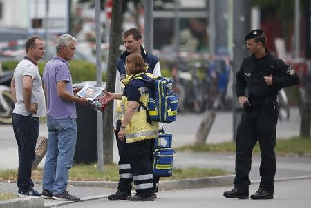 A man holding a photo he claims is his son who was killed in yesterday's shooting rampage, speaks to emergency care team members near the Olympia shopping mall, where the attack started in Munich, Germany July 23, 2016. REUTERS/Michael Dalder