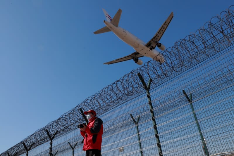 A man wearing a protective mask stands at a fence surrounding Beijing Capital International as a plane lands in Beijing as the country is hit by an outbreak of the novel coronavirus