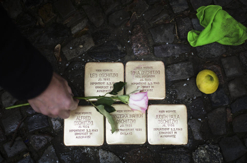 FILE - Local resident Juergen Schulz lays down a flower after he polishes so-called 'Stolpersteine' or 'stumbling stones' commemorating people deported and killed by the Nazis in front of his house in Berlin, Germany, Nov. 9, 2021. Holocaust survivors from around the world are warning about the reemergence of antisemitism as they commemorated Wednesday, Nov. 9, 2022, the 84th anniversary of the Kristallnacht or the "Night of Broken Glass", when Nazis terrorized Jews throughout Germany and Austria. (AP Photo/Markus Schreiber, File)