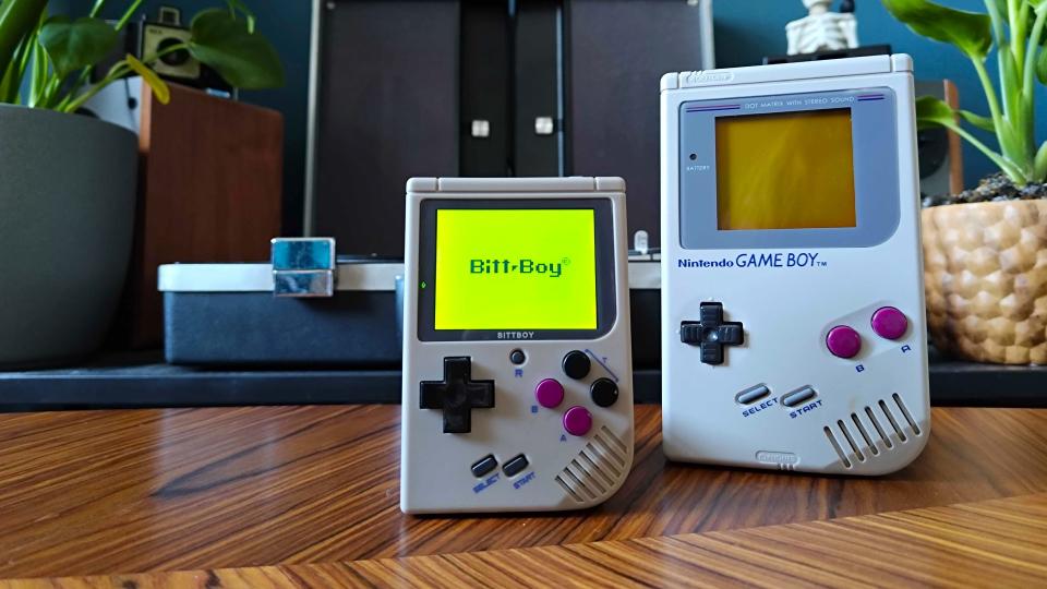 Bittboy handheld next to Game Boy on woodgrain table