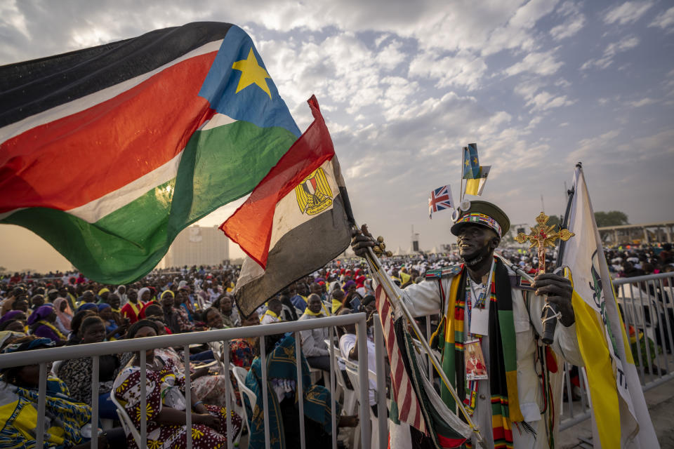 A man holds flags next to the audience as they await the arrival of Pope Francis for a Holy Mass at the John Garang Mausoleum in Juba, South Sudan Sunday, Feb. 5, 2023. Pope Francis is in South Sudan on the final day of a six-day trip that started in Congo, hoping to bring comfort and encouragement to two countries that have been riven by poverty, conflicts and what he calls a "colonialist mentality" that has exploited Africa for centuries. (AP Photo/Ben Curtis)