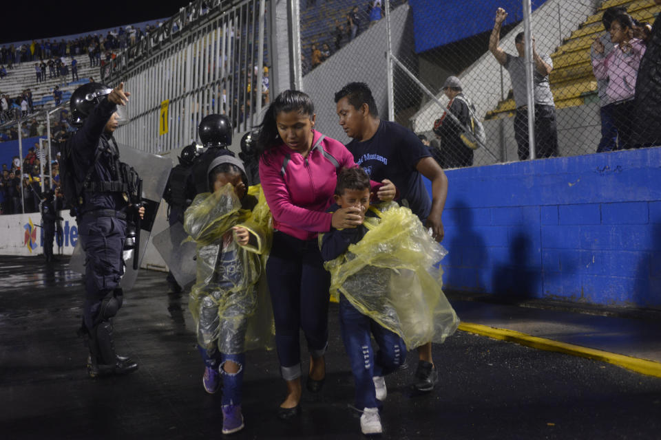 A family enters the perimeter of the soccer field to run away from tear gas that was fired by police to break up deadly fights, before the start of a game between the Motagua and Olimpia soccer teams at the national stadium in Tegucigalpa, Honduras, late Saturday, Aug. 17, 2019. The fight between fans of rival soccer teams outside the stadium left three people dead and led to the suspension of the game. (Victor Colindres/La Tribunal via AP)