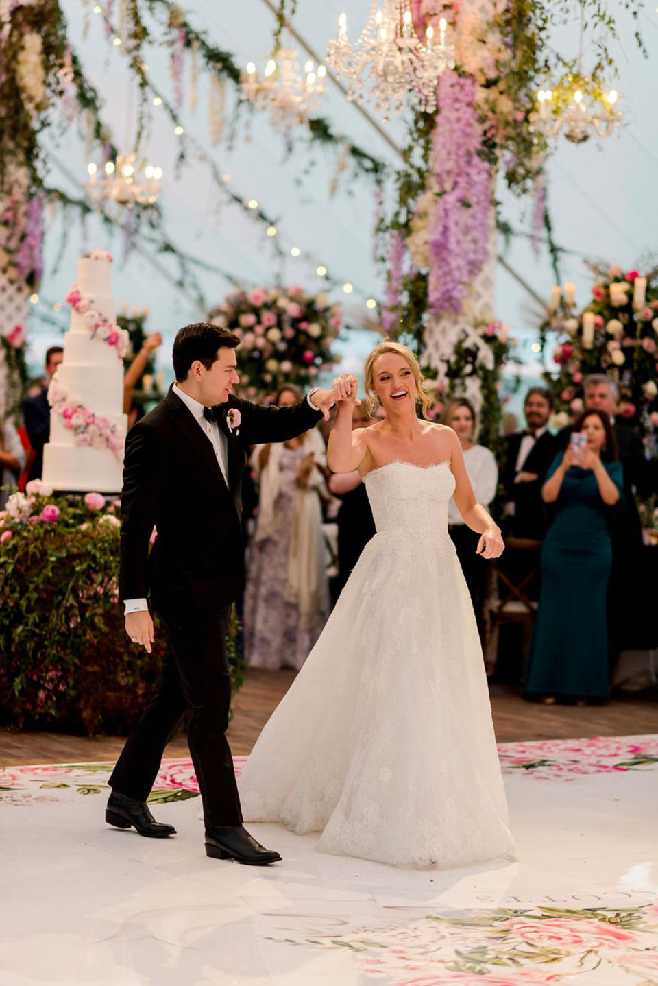 Alex Drummond in a white wedding gown dances with her new husband in a black suit on a dance floor under hanging purple flowers (Courtesy of Ashley Alexander Photography)