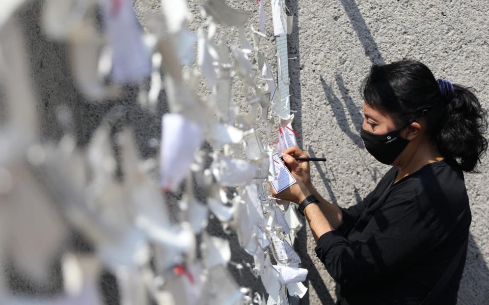 A woman places a message dedicated to people who died with Covid-19, on a wall at the Basilica of Guadalupe in Mexico City - Sashenka Gutierrez/EPA-EFE/Shutterstock