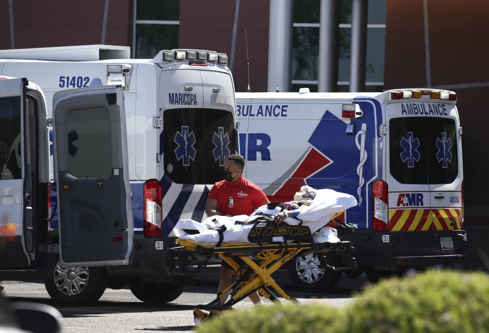 A person is brought to a medical transport vehicle from Banner Desert Medical Center as several transports and ambulances are shown parked outside the emergency room entrance, Tuesday, June 16, 2020, in Mesa, Ariz. (AP Photo/Ross D. Franklin)