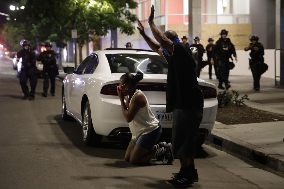 A woman and man duck behind a car as they are surrounded by police officers Sunday, May 31, 2020, in Los Angeles, during protests over the death of George Floyd. (AP Photo/Jae C. Hong)