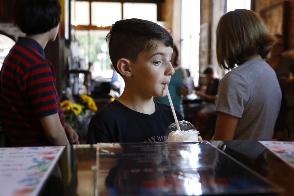 In this Friday, July 26, 2019 photo, Ethan Curtis, a 10-year-old Stranger Things fan from San Antonio, eyes the Stranger Drinks menu while sipping on a Sheriff Hopper specialty drink at Lucy Lu's Coffee Cafe in Jackson, Ga. Behind him, family members Emilynn Guthrie, 9, and Layla Curtis, 13, are dressed like characters Mike and Eleven from Stranger Things. Lucy Lu's employees said the themed menu is popular among locals and fans who visit to see filming locations. (AP Photo/Andrea Smith)