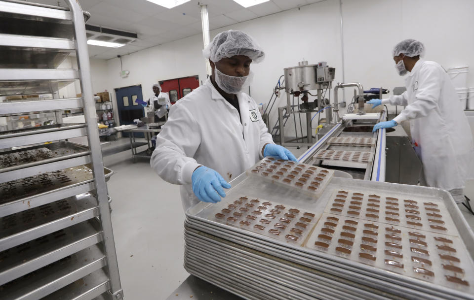 Michael Tyus, left, and Alem Berhane make cannabis-infused chocolate toffee candies at Evergreen Herbal, Wednesday, July 24, 2019, in Seattle. Washington state's marijuana regulators have eased some requirements regarding the "seed to sale" tracking of the drug, a week after a botched software update began preventing many business from being able to ship their products, cost hundreds of thousands of dollars in lost sales and prompted some to furlough workers. (AP Photo/Elaine Thompson)