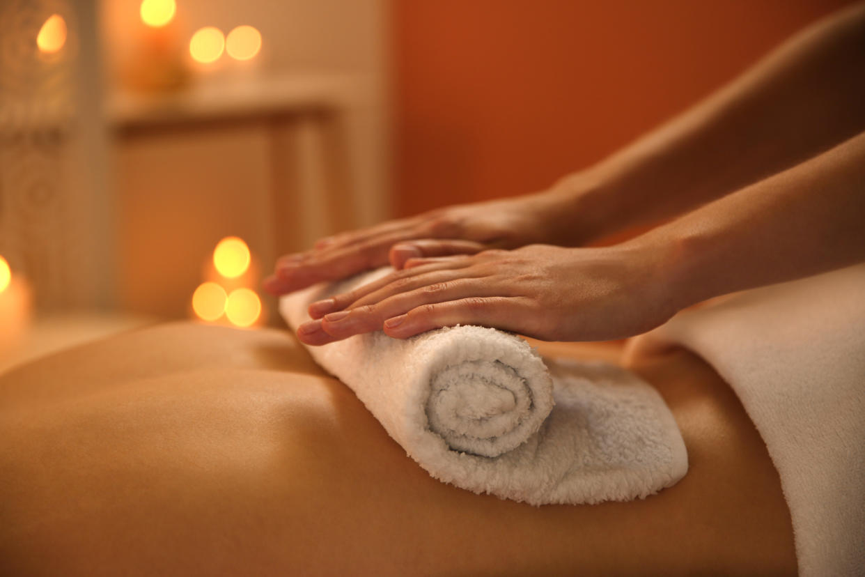 Woman unrolling a hot towel across another woman's exposed back. 