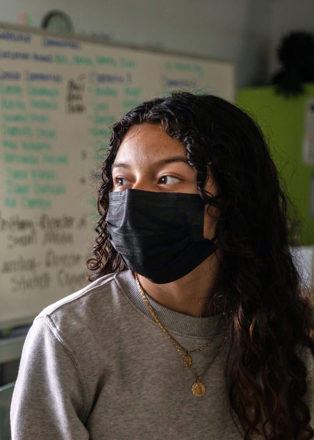 A high school girls wears a face mask, looking off to the left.