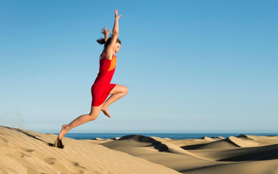 Laughing girl jumping at sunset from sand dune with arms wide open - some motion blur. I took a leap of faith – and look where it landed me: the Maspalomas Dunes, of Gran Canaria -  Kemter