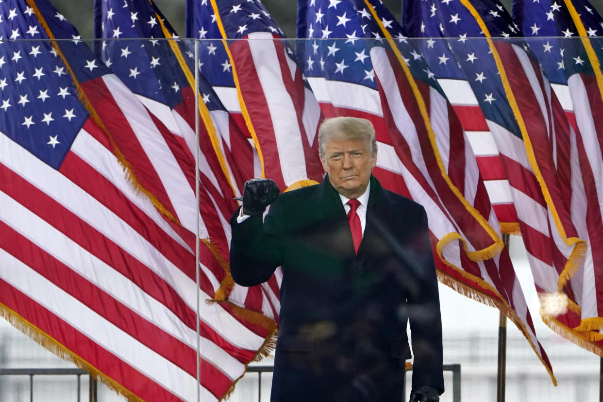 Donald Trump stands behind a protective transparent barrier while onstage at a rally.