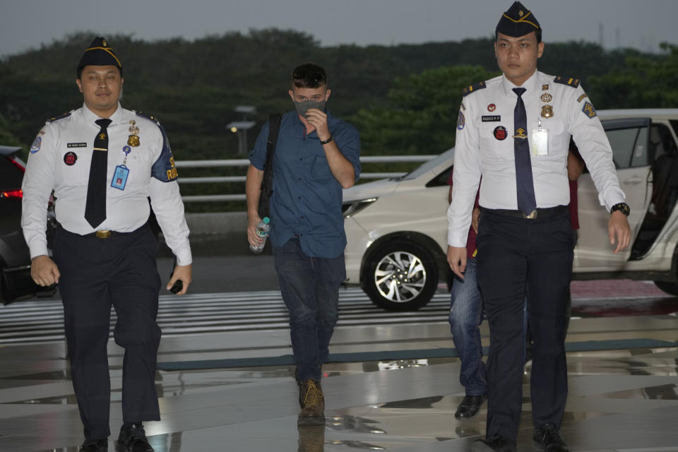 Australian national Bodhi Mani Risby-Jones from Queensland, center, is escorted by immigration officers upon arrival at Soekarno-Hatta International Airport in Tangerang, Indonesia, Saturday, June 10, 2023. Indonesia’s authorities are deporting an Australian surfer who apologized for attacking several people while drunk and naked in the deeply conservative province of Aceh. Bodhi Mani Risby-Jones was detained in late April on Simeulue Island, a surf resort, after police accused him of going on a drunken rampage that left a fisherman with serious injuries. (AP Photo/Dita Alangkara)