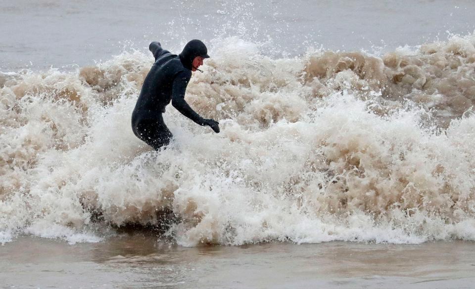 A surfer starts a surf in a torrent of waves, Saturday, December 12, 2020, in Sheboygan, Wis.