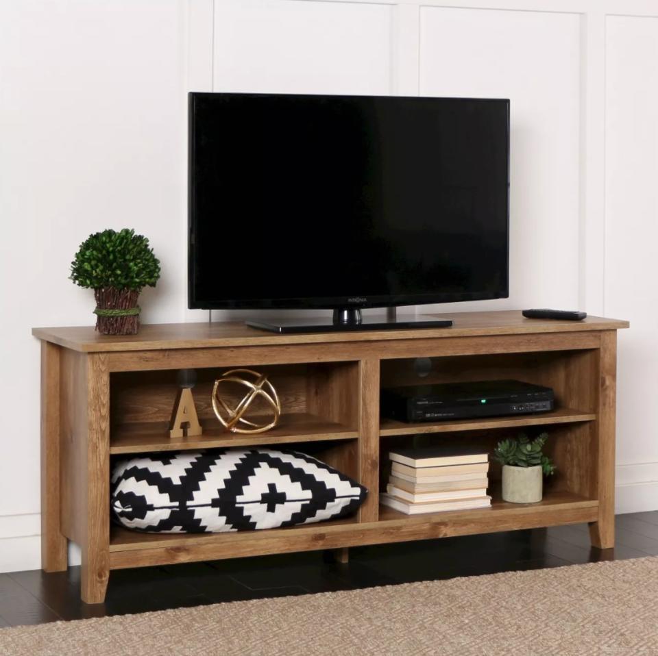The rustic wood TV stand holding a flat-screen, pillows, books, and plants