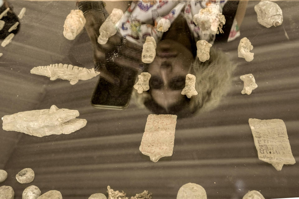 A visitor is reflected on a panel on which recently unearthed ancient artifacts are placed, as she films at the site of the Step Pyramid of Djoser in Saqqara, 24 kilometers (15 miles) southwest of Cairo, Egypt, Saturday, May 27, 2023. Saqqara is a part of Egypt's ancient capital of Memphis, a UNESCO World Heritage site. (AP Photo/Amr Nabil)