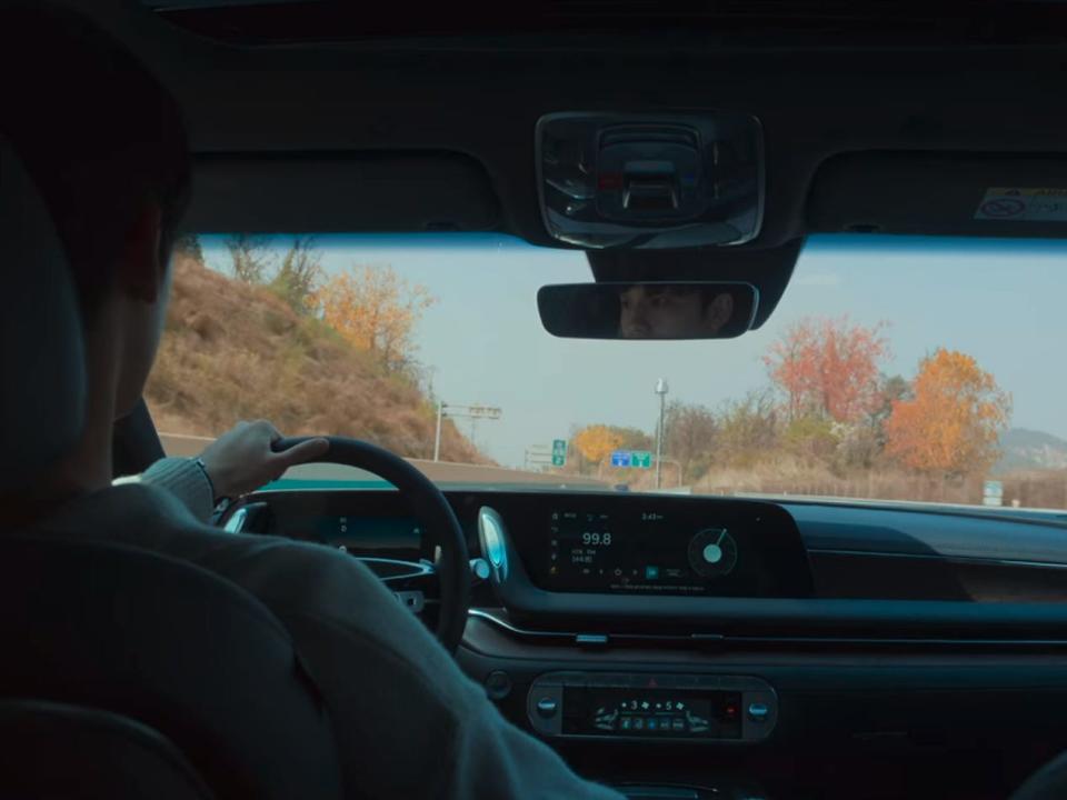 yeo-jeong listening to the radio in his car, driving on the road with autumn leaved trees