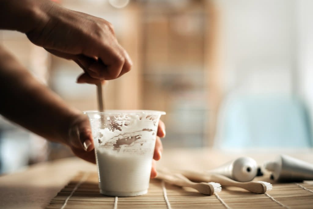 A woman makes DIY toothpaste in a plastic cup.